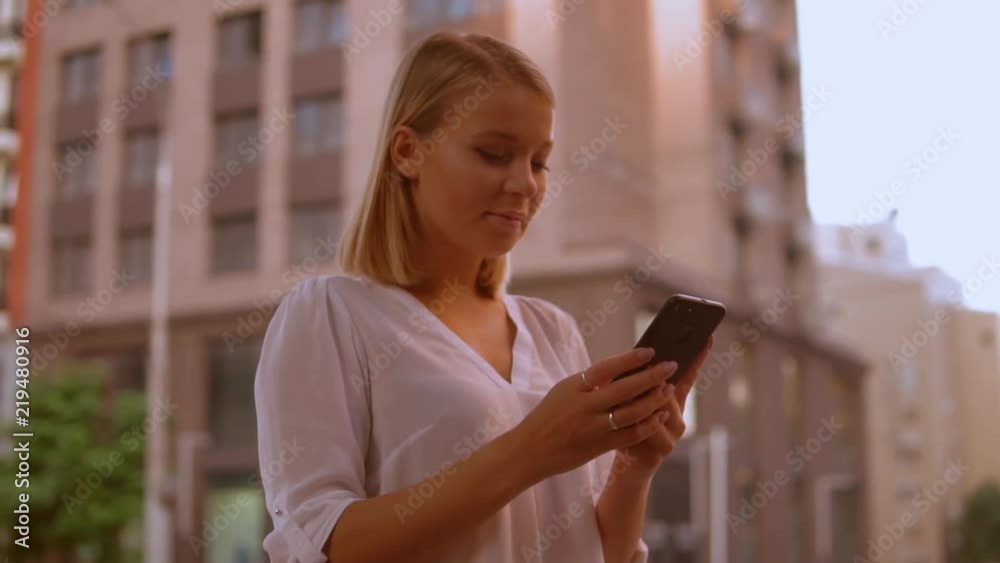 successful businesswoman using mobile phone texting message standing on the street beautiful modern city. caucasian woman wearing elegant white shirt. slow motion successful businesswoman using mobile phone texting message standing on the street beautiful modern city. caucasian woman wearing elegant white shirt. slow motion