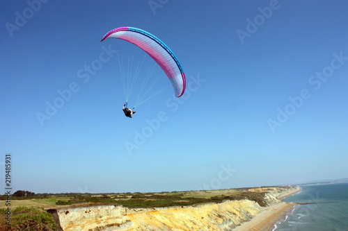 man is flying on white paraglider in the sky above the blue sea. Balance, extreme sports, active lifestyle. English canal, Barton-on-sea, England