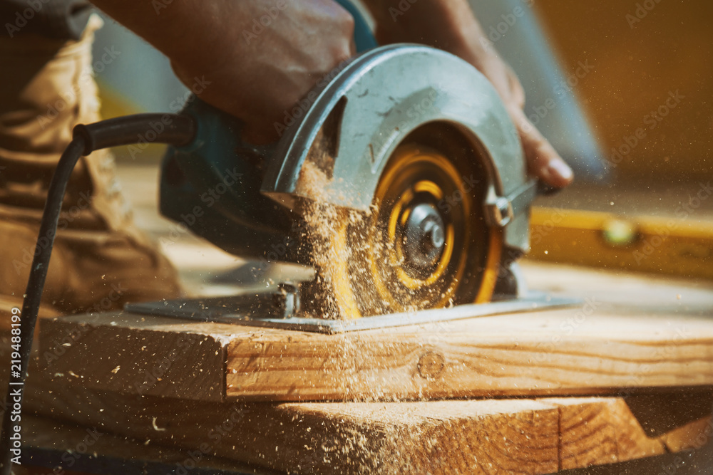 Close-up of a carpenter using a circular saw to cut a large board of wood - obrazy, fototapety, plakaty 