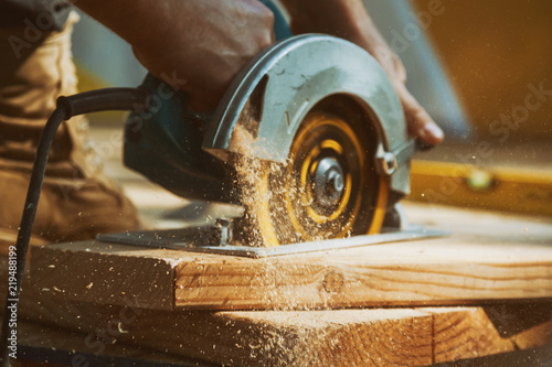 Fotografering Close-up of a carpenter using a circular saw to cut a large board of wood