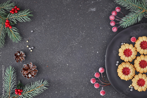 Flat lay with Xmas decorations in green and red and jam cookies on dark grey