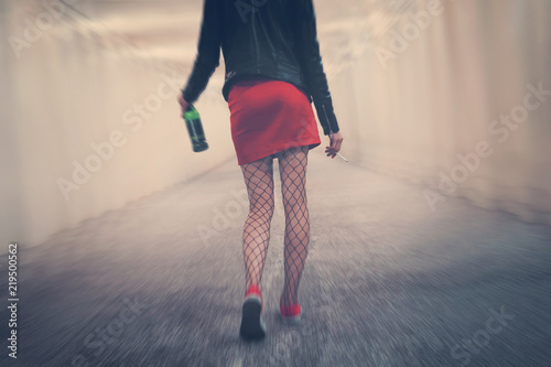 drunk woman with cigarette and bottle goes into distance along corridor stumbling and falling. Young girl in red skirt tights walk away. concept alcoholism bad habits. Blur effect showing dizziness photo