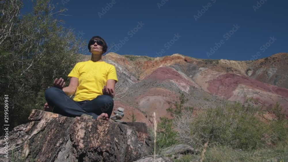 A female traveler sits on a huge tree stump and meditates against the beautiful mountains. A female traveler sits on a huge tree stump and meditates against the beautiful mountains.