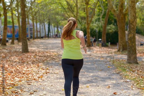 Back view of a plump middle-aged woman running through a park