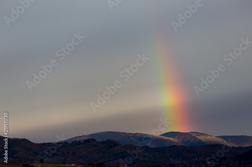 Beautiful and surreal view of part of a rainbow over some hills © Massimo