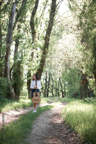 young woman walking in the forest and playing guitar, summer nature, bright sunlight, shadows and green leaves, romantic feelings © soleg