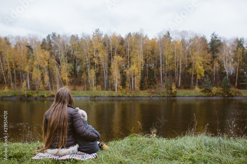 Mother and son sitting at the river bank in autumn © Natasha