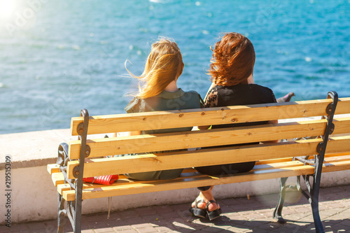 two friends sitting on a bench overlooking the sea