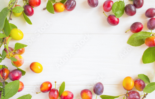 frame with fresh plums with leaves on white rustic wooden table. The concept of autumn harvest.