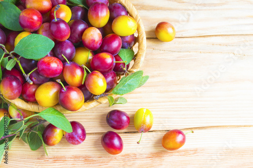 Fresh plums with leaves in a basket on a rustic wooden table top view. The concept of autumn harvest.