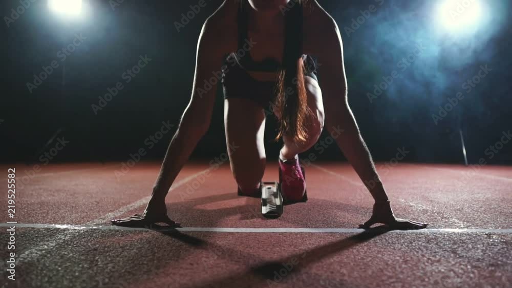Professional woman athlete on a dark background gotovtes to run the sprint of Jogging shoes in sneakers on the track of the stadium on a dark background. Close up