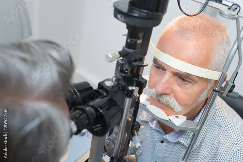 senior man looking into slit lamp at clinic
