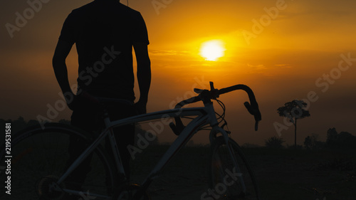 Fototapeta Naklejka Na Ścianę i Meble -  Silhouette man standing outdoor with a bike on sunset.
