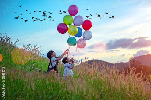 group of Happy little girls holding colorful balloons. Child playing on a green meadow. Smiling kid, beautibull sky sunset and flock of bird in backbround