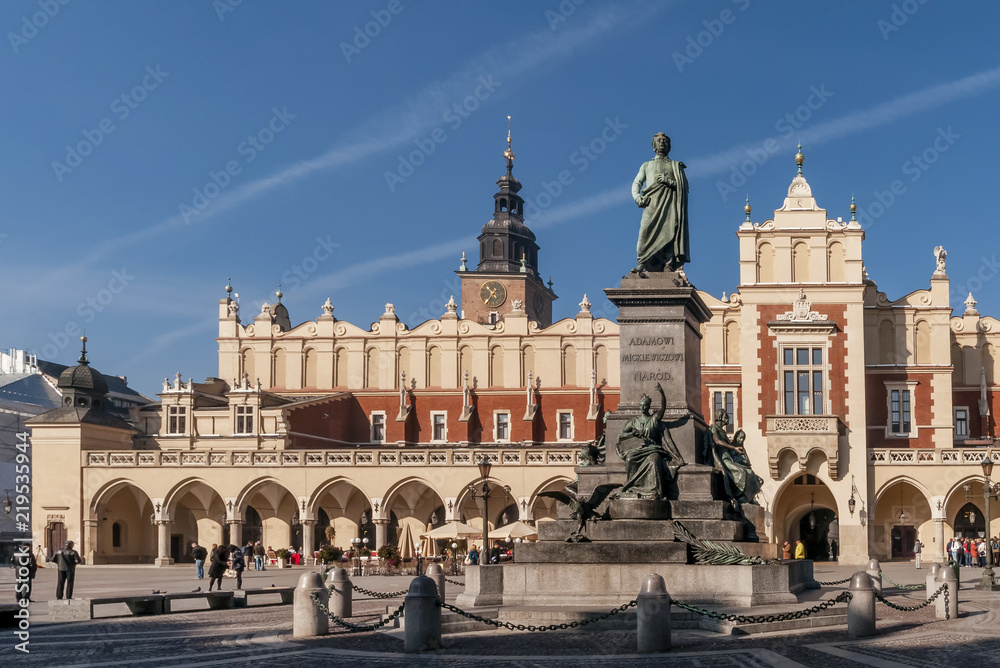 Obraz premium The Adam Mickiewicz statue and the Cloth Hall in the historic center of Krakow, Poland on a beautiful sunny day