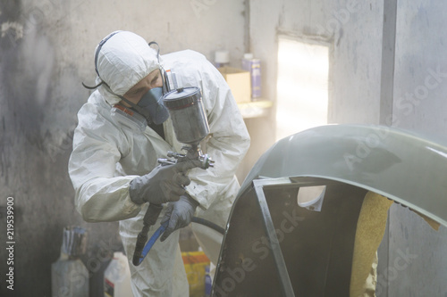 auto mechanic worker painting car in a paint chamber during repair work