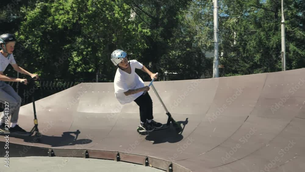 A young guy jumps and does tricks on a scooter in a skatepark