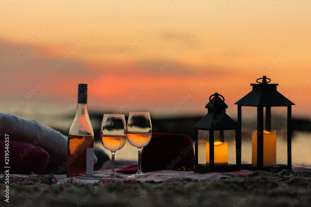 Summer sea sunset. Romantic picnic on the beach. Bottle of wine, glasses, candles, plaid and pillows. - obrazy, fototapety, plakaty 