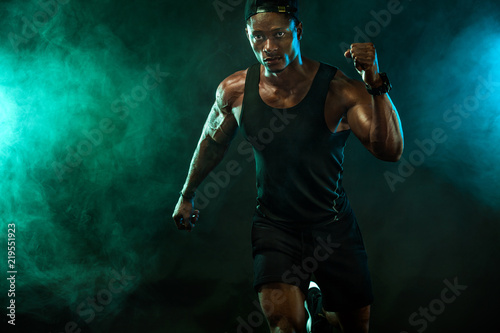 Sports men athlete runner on dark background. Power athletic guy bodybuilder doing fitness training. Man sprinter.