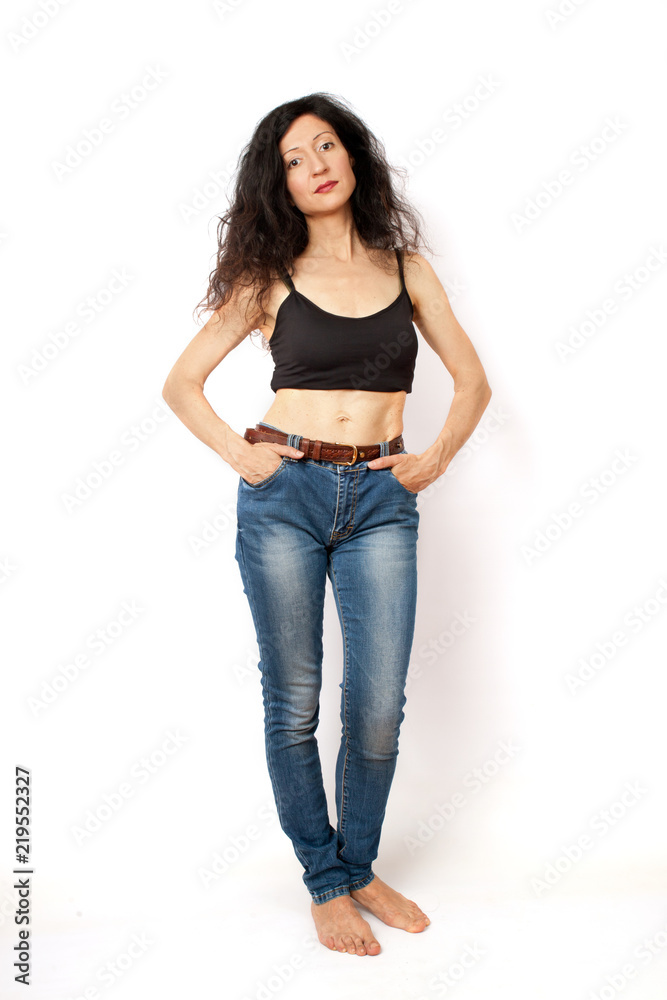 Cheerful slim curly brunette woman standing in blue jeans and a