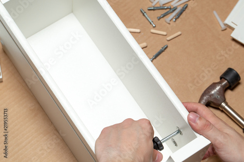 Assembling of furniture, closeup of tool in hand. Mounting screw is screwed into hole board.