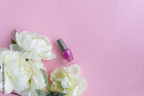 Pink background with white peonies and nail polish on the side. Copy space
