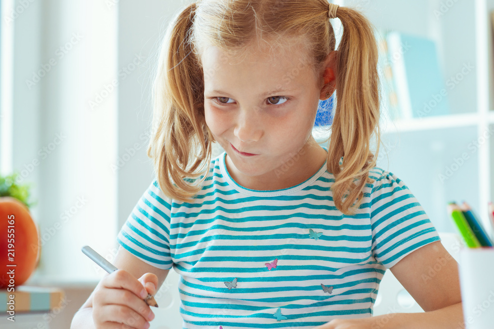 Portrait of a thoughtful cute girl sitting at a table with books in a light classкroom Portrait of a thoughtful cute girl sitting at a table with books in a light classкroom