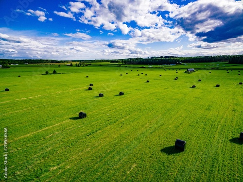 Aerial view of round straw bales in black plastic in green field in rural Finland.