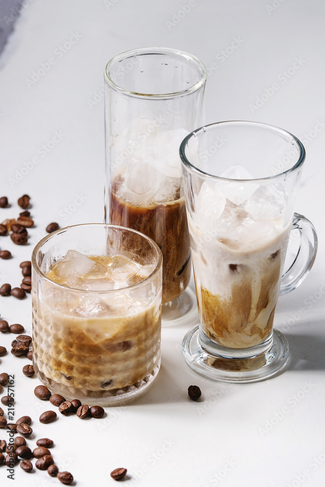 Iced coffee cocktail or frappe with ice cubes and cream served in three different glasses with coffee beans around on white marble table. Iced coffee cocktail or frappe with ice cubes and cream served in three different glasses with coffee beans around on white marble table.