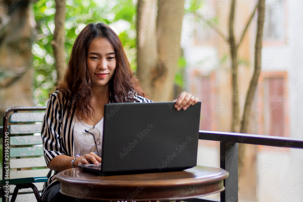 Young freelance woman using laptop to work outside coffee shop. Business person using laptop to communicate. Female student using laptop and study outside cafe in free time.