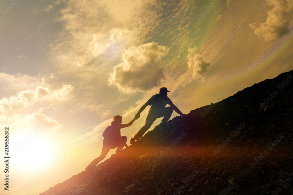 Fototapeta premium Silhouettes of a man helping a girl climb a mountain. against the background of sunset. Business idea, teamwork, cooperation. Success and Achievements