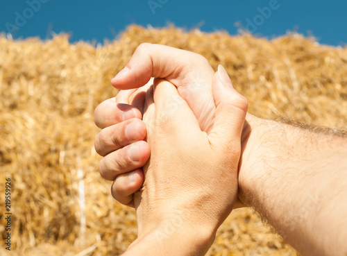 The hands of a man and a woman are woven together against a background of straw and a blue sky in the summer, ideal for an inscription or background