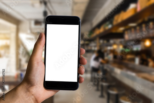 Hands holding a white mobile phone with a blank white screen in the corner of the cafe..