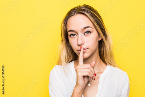 Girl showing silence sign isolated on yellow background