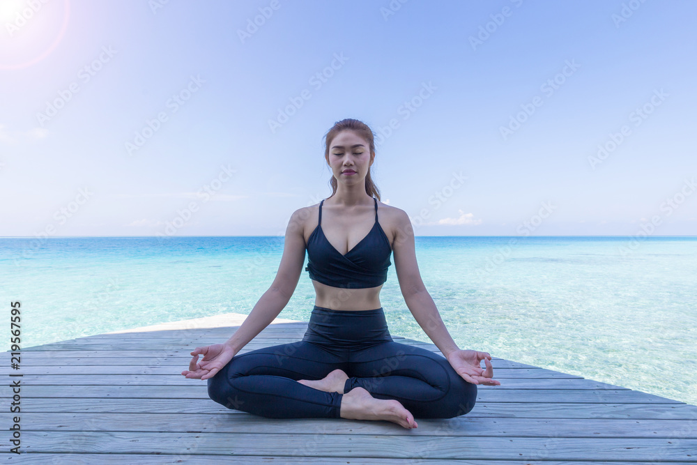 Asian woman wearing black sportswear practicing yoga Lotus pose for meditation and warm up on the beach in Maldives at sunset,Feeling so comfortable and relax in holiday,Healthy Concept Asian woman wearing black sportswear practicing yoga Lotus pose for meditation and warm up on the beach in Maldives at sunset,Feeling so comfortable and relax in holiday,Healthy Concept