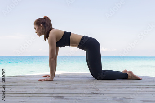 Asian woman wearing black sportswear relaxing in yoga Child's Pose stretching exercises muscle for warm up on beach in Maldives with seaside,Feeling so comfortable and relax in holiday,Healthy Concept