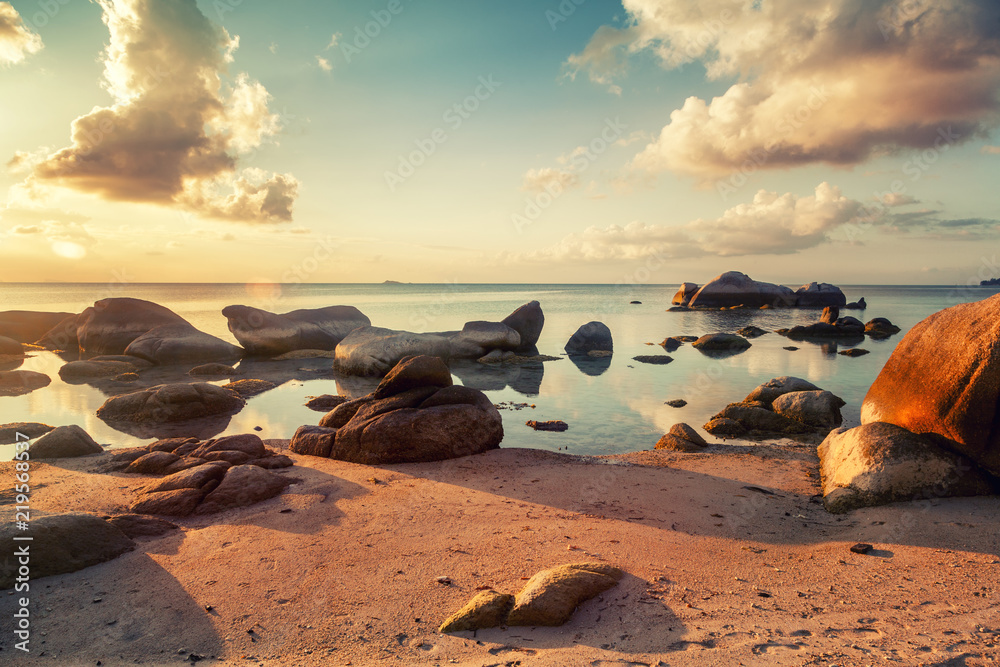 bright tropical beautiful landscape, sunset on the beach with large stones, clouds reflected in the water