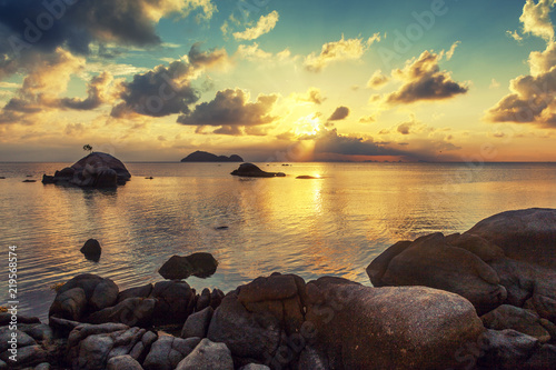 bright tropical beautiful landscape, sunset on the beach with large stones, clouds reflected in the water