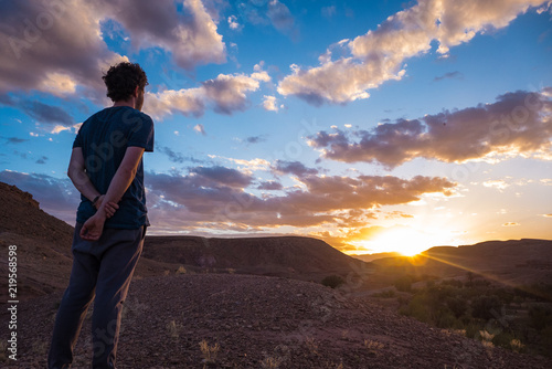 A young man watching the sunset in a beautiful valley. Some clouds in the sky, Beginning, reflection, relaxing, meditating, peaceful, insights concepts.