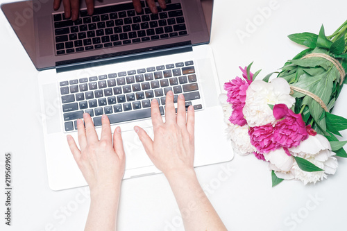 Workplace with laptop female hands notebook pink white peony flowers