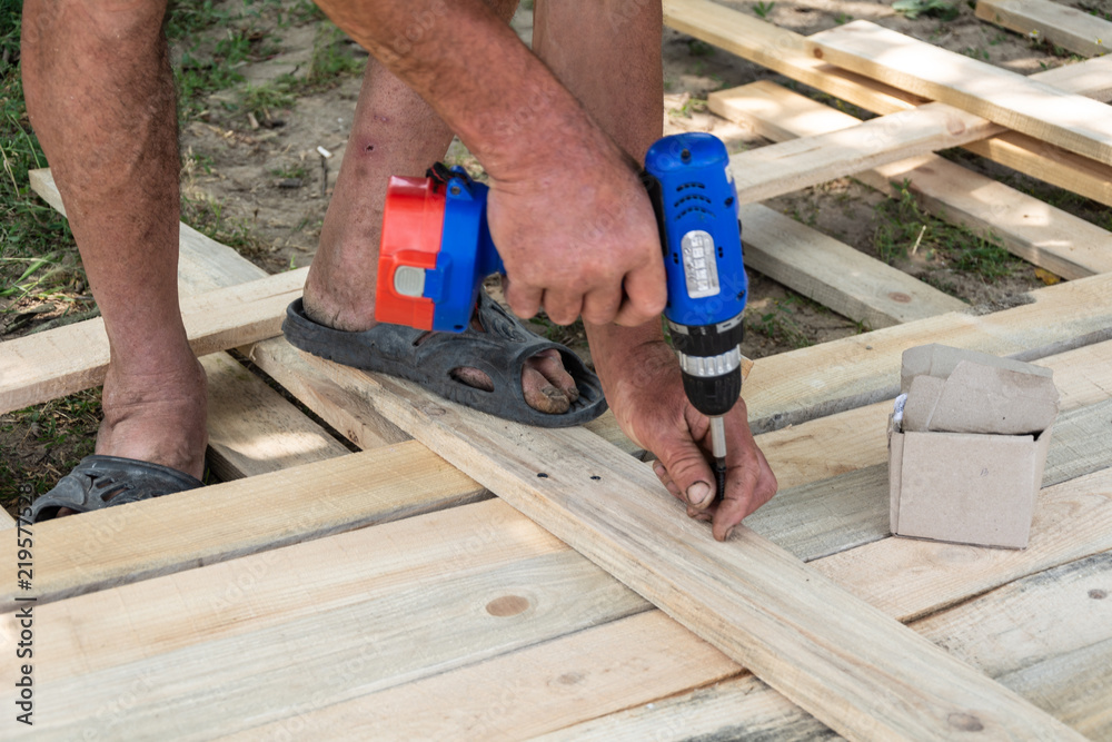 Drill wood workshop. Woodwork and people concept - carpenter with battery power drill drilling wood plank at workshop, Formwork for the fence Drill wood workshop. Woodwork and people concept - carpenter with battery power drill drilling wood plank at workshop, Formwork for the fence