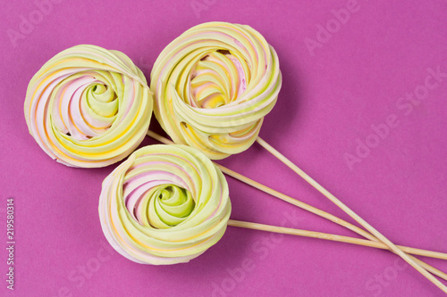 three round meringue on a stick lie on a dark pink background, the concept of a holiday and dessert