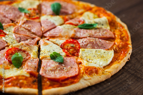 sliced Pizza with Mozzarella cheese, Ham, Tomatoes, pepper, Spices and Fresh Basil. Italian pizza on wooden background