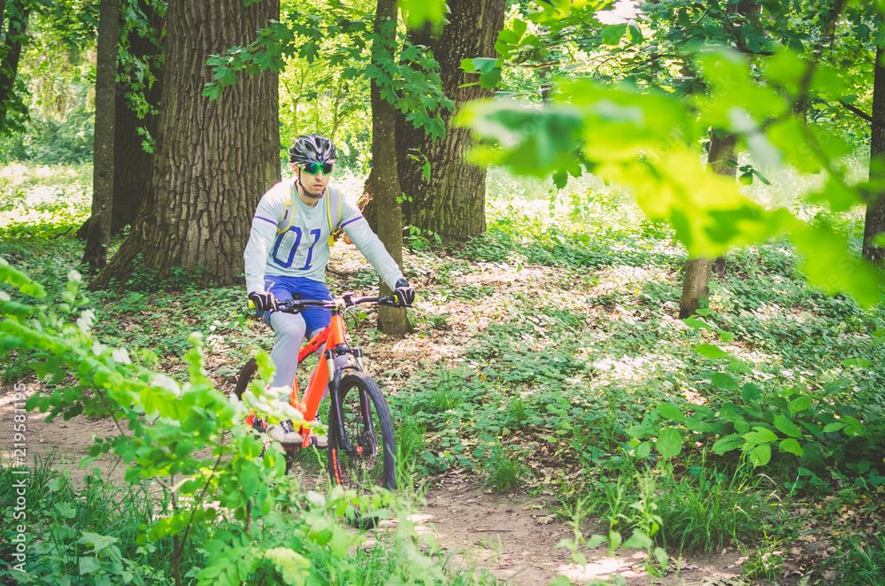 Cyclist in helmet on orange bike riding in park Cyclist in helmet on orange bike riding in park