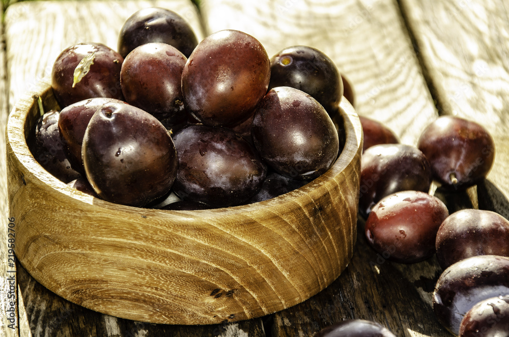 Obraz premium Vintage plums in a wooden bowl, on a wooden background, on the grass on a sunny afternoon on the grass.