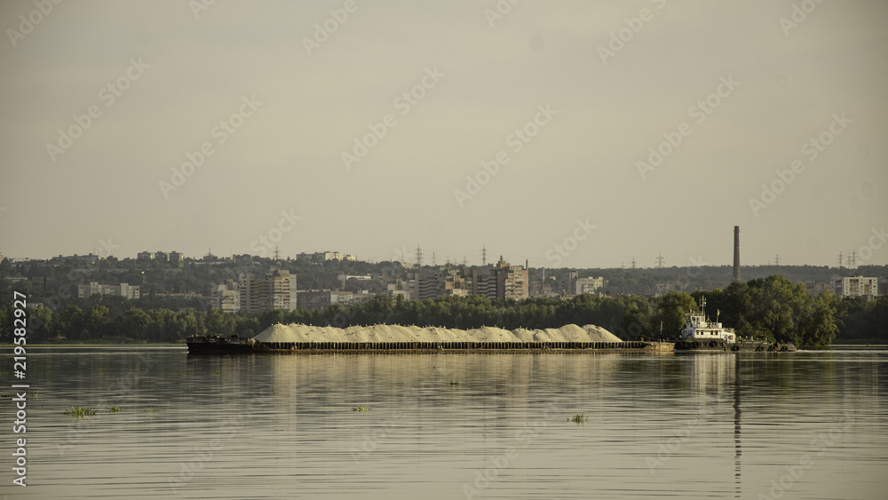 Barge with sand on the river, in the summer, against the backdrop of the city.