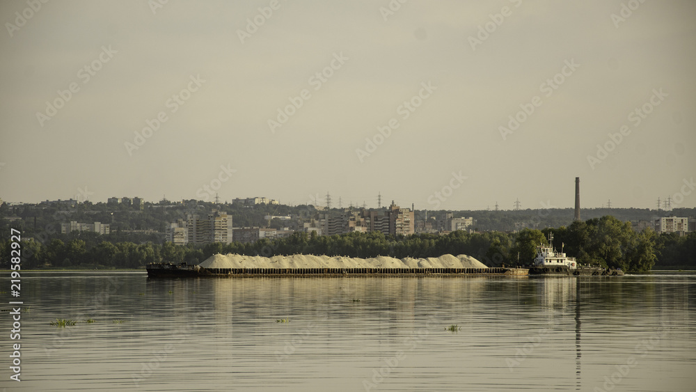 Obraz premium Barge with sand on the river, in the summer, against the backdrop of the city.