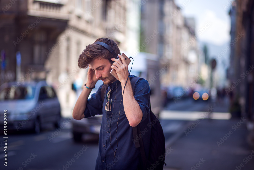 Portrait of handsome young man with cell phone and headphones listening to music on the street