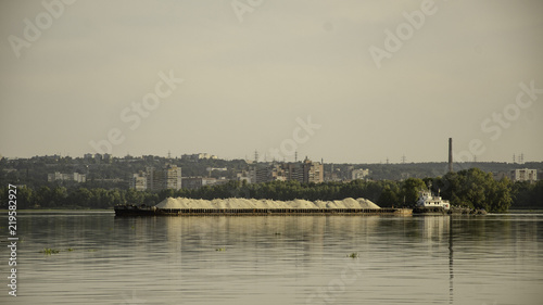 Barge with sand on the river, in the summer, against the backdrop of the city. © YUABOG