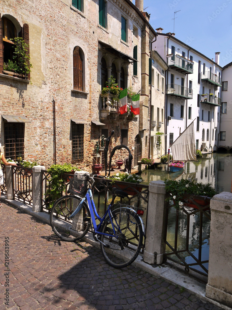 A bicycle rests upon railings of a bridge over a river in Treviso Italy